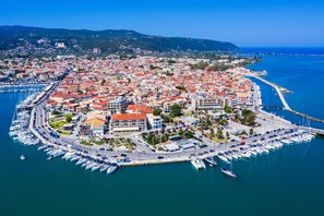 An aerial view of a coastal town with a marina, red-roofed buildings, and a clear blue sea.