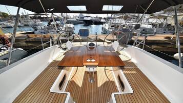 A boat deck with a wooden table, two steering wheels, and a view of other boats in a marina.