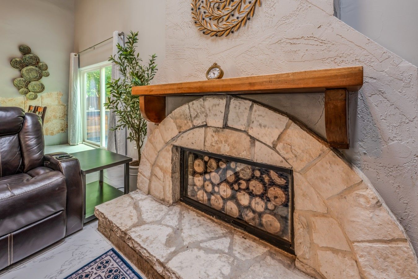 A stone fireplace with a wooden mantel, a leather sofa, and a decorative wall piece.