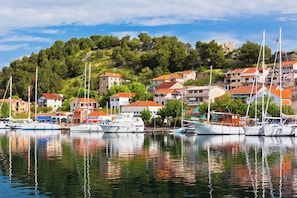A marina with boats docked, buildings with red roofs, and a hillside with trees. - Sibenik Sun and Beach Sailing Extravaganza (Skradin)