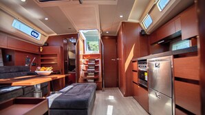 A compact kitchen with a built-in oven, a dining area with a bench, and a small seating area with a bowl of fruit. - Sun-kissed Sailing Adventure in the Ionian Islands (Preveza)