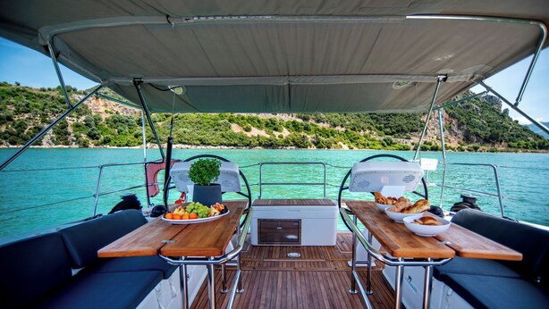 A boat deck with two tables, a potted plant, and a view of a coastline. - Sun-kissed Sailing Adventure in the Ionian Islands (Preveza)
