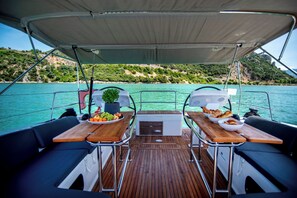 A boat deck with two tables, a potted plant, and a view of a coastline. - Sun-kissed Sailing Adventure in the Ionian Islands (Preveza)
