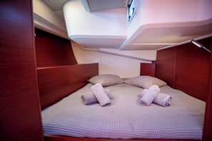 Ein kleines, helles Quartier mit einem Einzelbett, Kissen und ordentlich zusammengelegten Handtüchern.