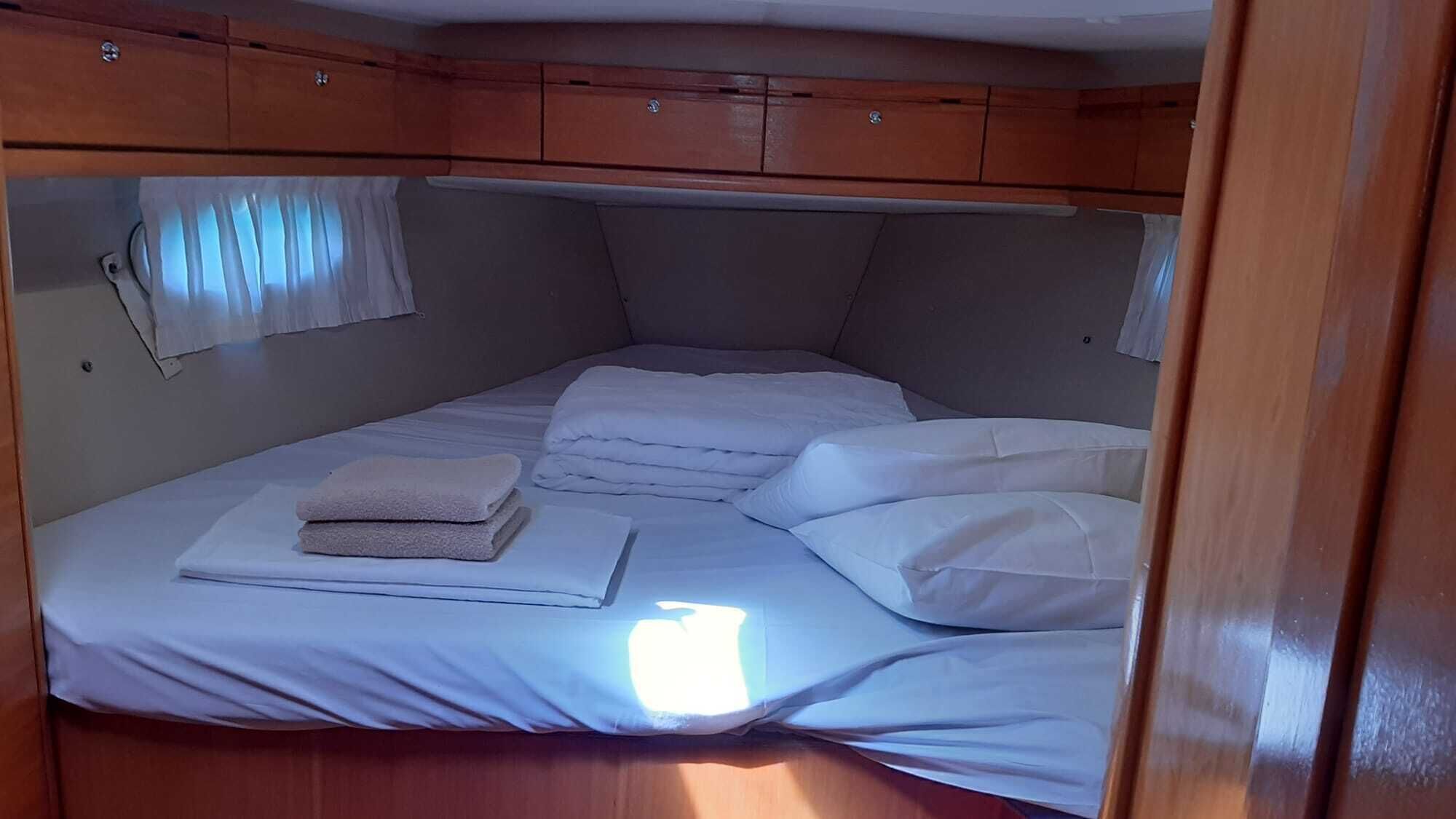 A compact, single-bed cabin with wooden cabinetry above and a window with curtains.