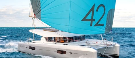 Um catamarã com uma grande vela azul marcada com o número 42 navegando no oceano.