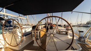 Le pont d’un bateau, avec deux roues de barre, un plancher en bois et une marina en arrière-plan.
