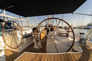 Ein Bootsdeck mit zwei Steuerhörnern, einem Holzboden und einem Yachthafen im Hintergrund.