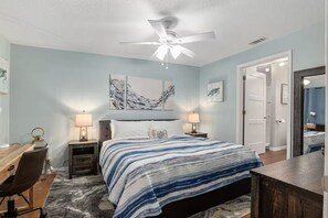 A bedroom with a bed, two bedside tables with lamps, a desk, a chair, and a ceiling fan. - Lake Rousseau Sunsets from Screen Porch + Firepit (Dunnellon)