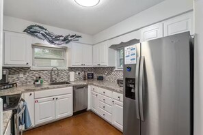 A modern kitchen with white cabinets, a stainless steel refrigerator, and a backsplash with a mosaic tile pattern. - Lake Rousseau Sunsets from Screen Porch + Firepit (Dunnellon)