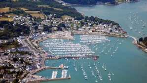 An aerial view of a coastal town with a marina filled with boats, surrounded by residential areas and a bridge connecting to the mainland. - Sun-Kissed Sailing Adventure in Golfo de Morbihan, Brittany (La Trinité-sur-Mer)
