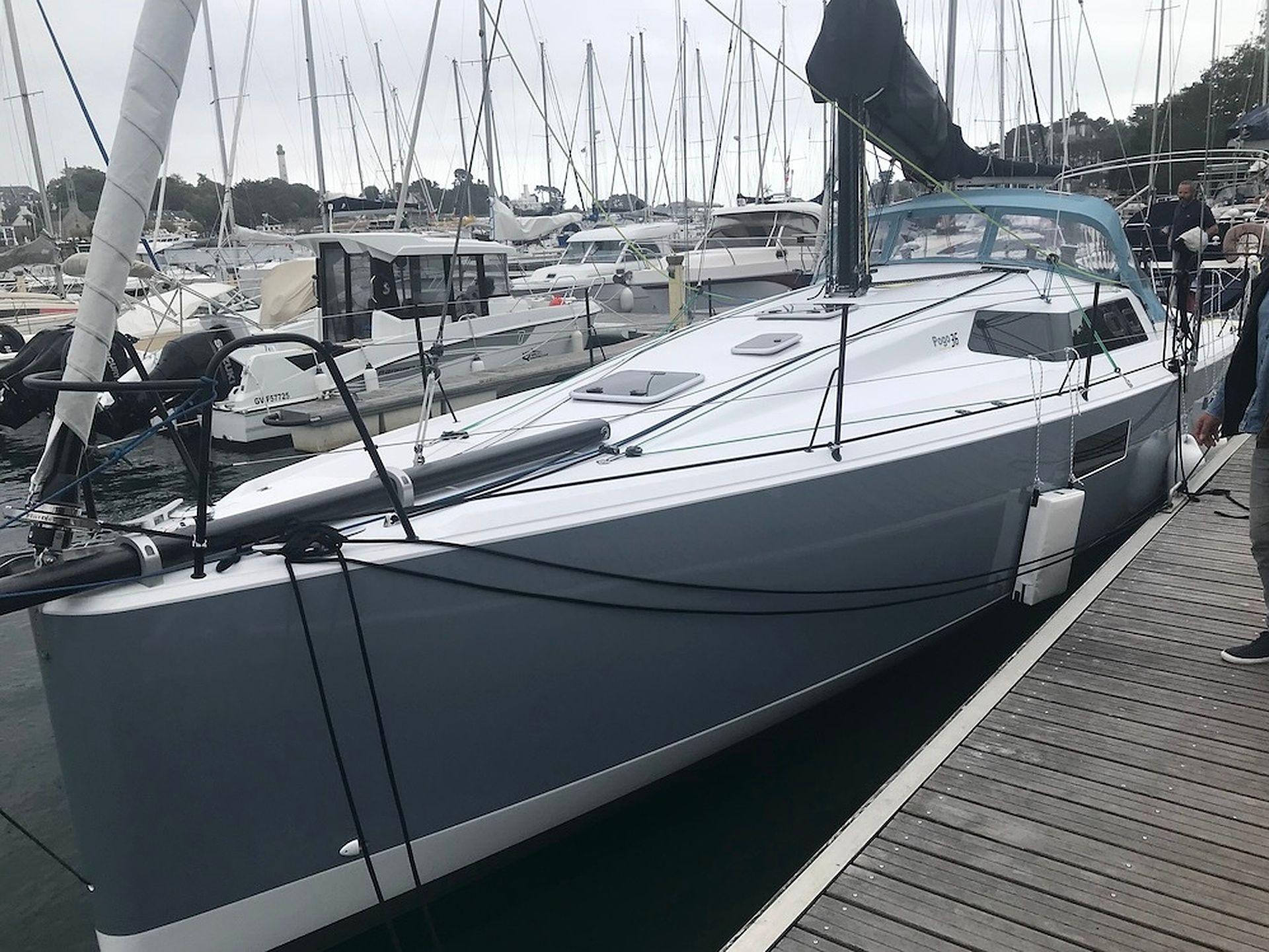 Un velero amarrado en un puerto deportivo junto a otras embarcaciones y una persona de pie en el muelle.