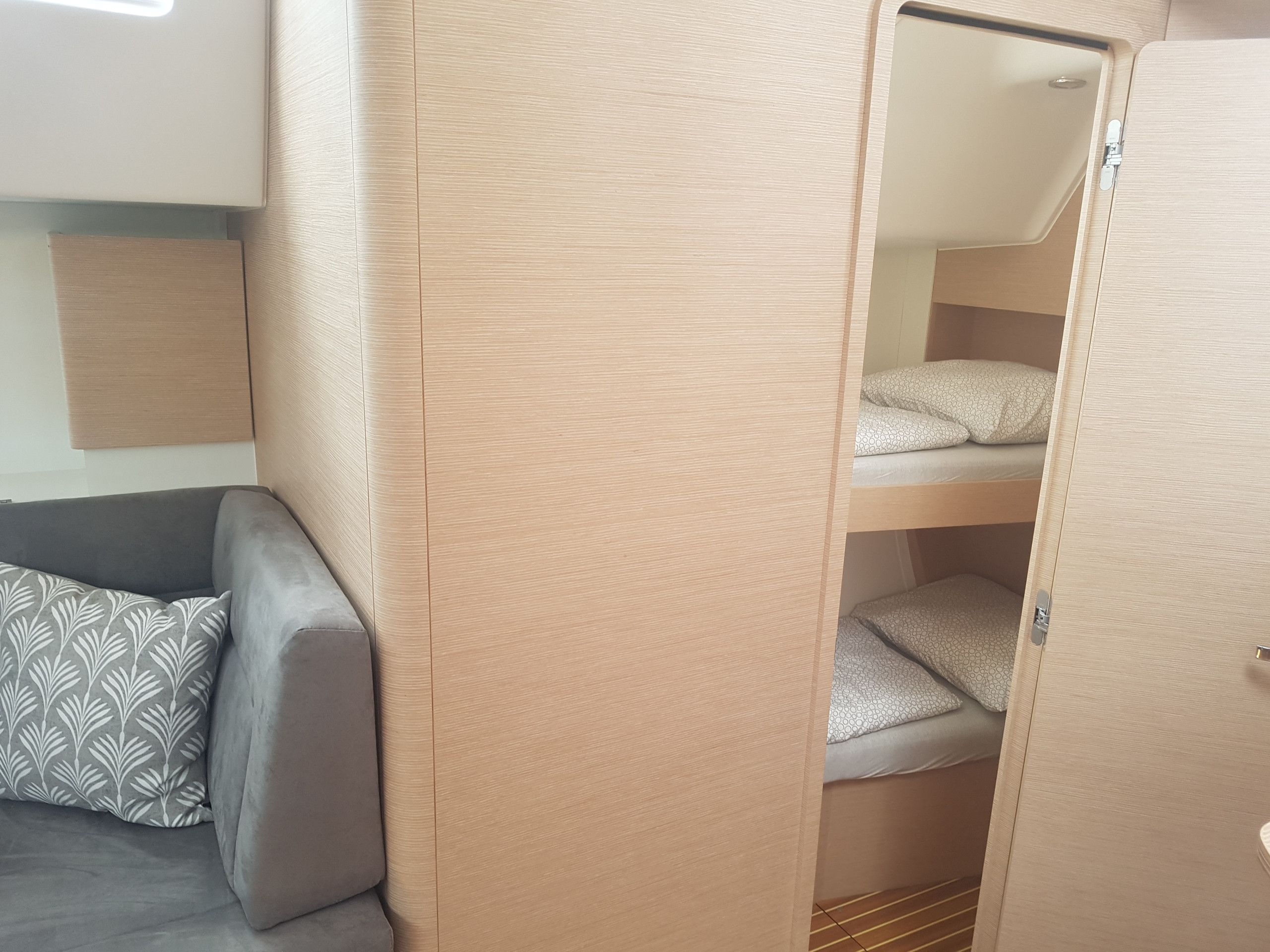 Una cama litera con cabecera, un sofá gris con cojines estampados y una puerta de madera.