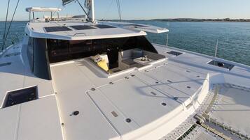 Cubierta de barco con asientos, un mástil y vista al agua.