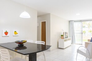 A modern kitchen with a dining table, white chairs, a black countertop, and a white pendant light. - Ocean Residence (Ipojuca)