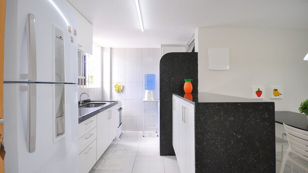 Eine moderne Küche mit weißen Schränken, einer schwarzen Kücheninsel und einem Kühlschrank.