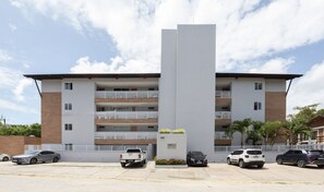 A multi-story residential building with a central vertical structure, balconies, and a parking area with cars. - Ocean Residence (Ipojuca)