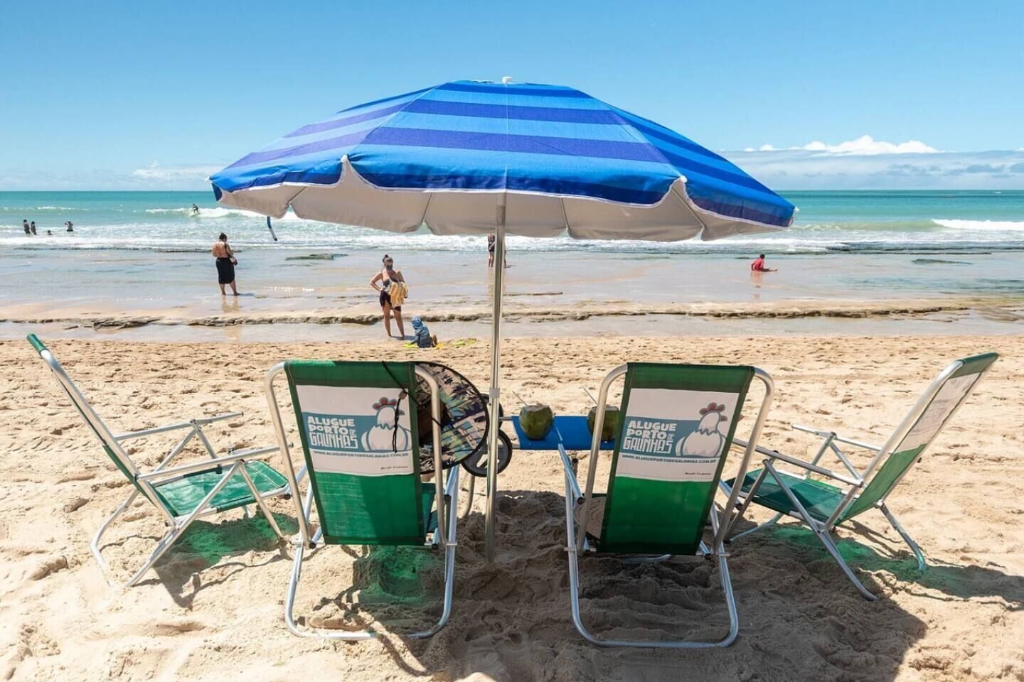 A beach with two green beach chairs under a blue and white striped umbrella, and the ocean in the background.