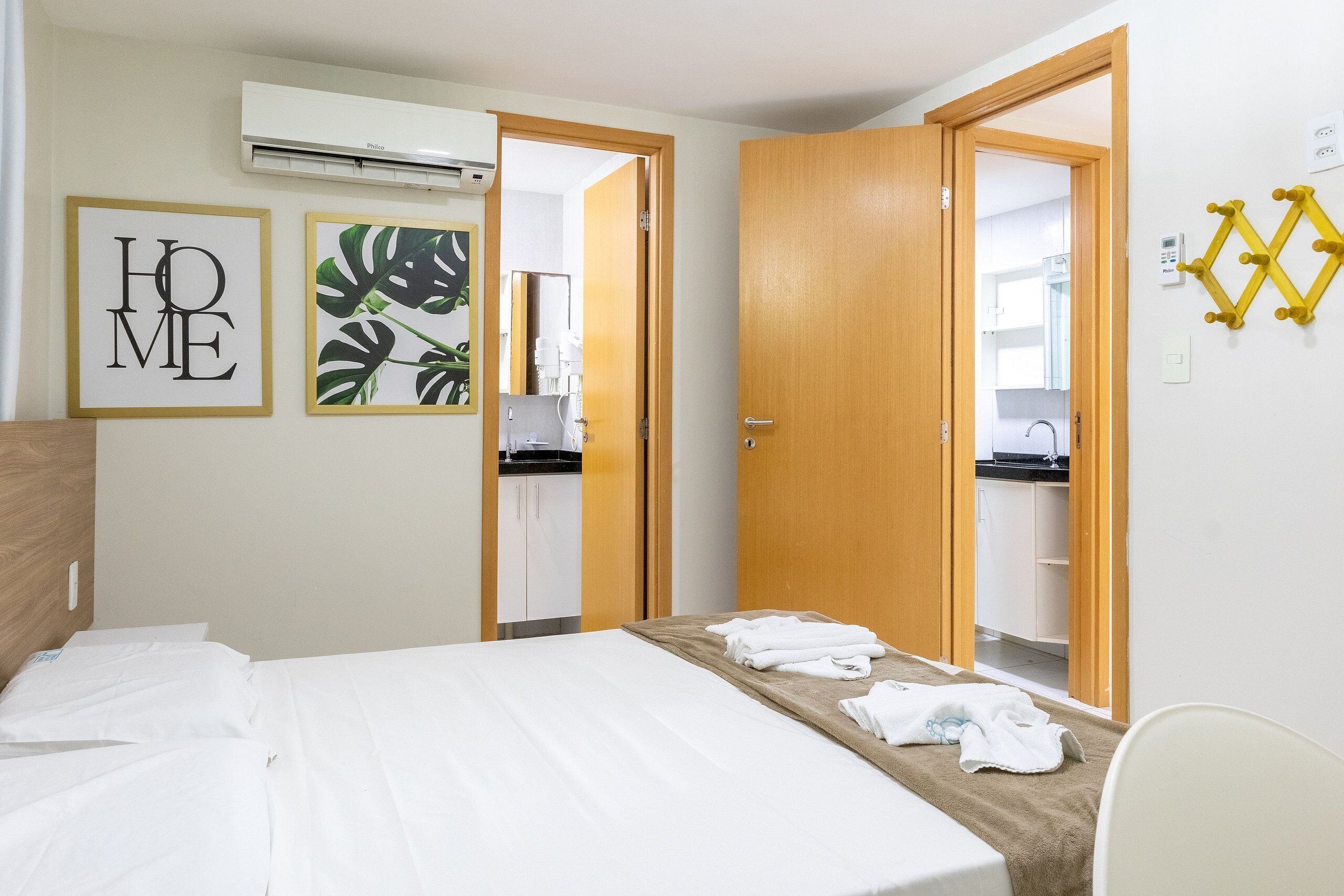 Quarto de hotel com uma cama, banheiro visível por uma porta aberta e ar-condicionado fixado na parede.