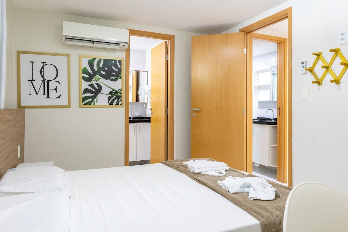 A hotel room with a bed, a bathroom visible through an open door, and a wall-mounted air conditioner.