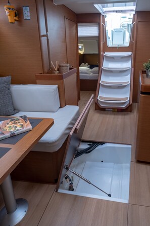A compact living space with a bed, a small table with a book, a bench, and a sliding shelf unit.