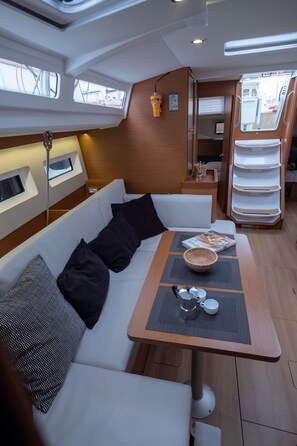 A compact boat interior with a seating area, a table with a coffee maker, and a small window.