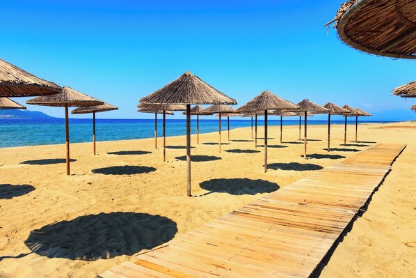 A beach with wooden walkways and thatched umbrellas.