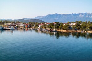 Un pueblo costero con barcos amarrados a la orilla, edificios de techos rojos y montañas al fondo.