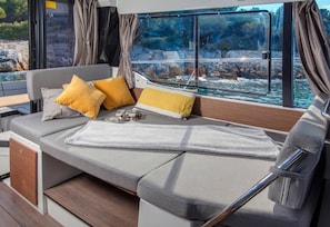 Eine gemütliche Sitzecke mit Kissen, einer Decke und Blick auf felsiges Gelände durch ein Fenster.