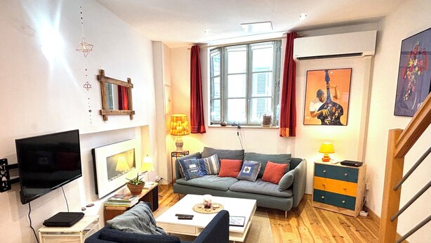 A living room with a flat-screen TV, a sofa, a coffee table, a lamp, a window with curtains, and a staircase. - Charming house in the historic district with a garage (Foix)
