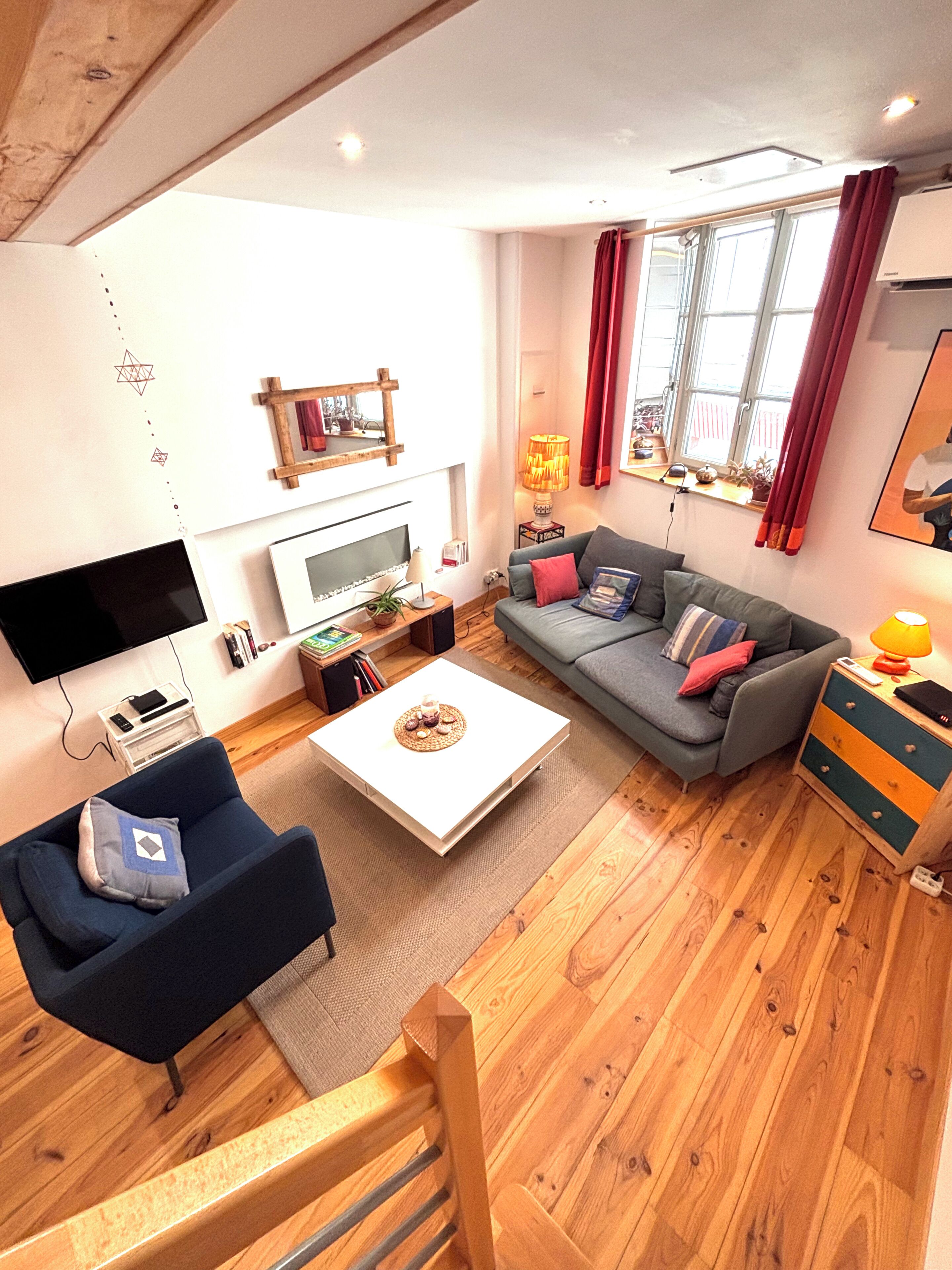 A modern living room with a flat-screen TV, a sofa, a coffee table, and a wooden floor.
