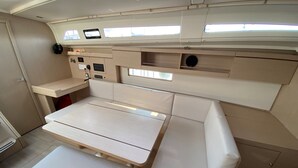 Een klein bootinterieur met een centrale tafel, comfortabele zitplaatsen en een bedieningspaneel.