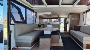 A yacht interior with a dining area, sofa, and a view of the marina. - Sun-Kissed Sailing Adventure in the Saronic Islands (Lavrio)