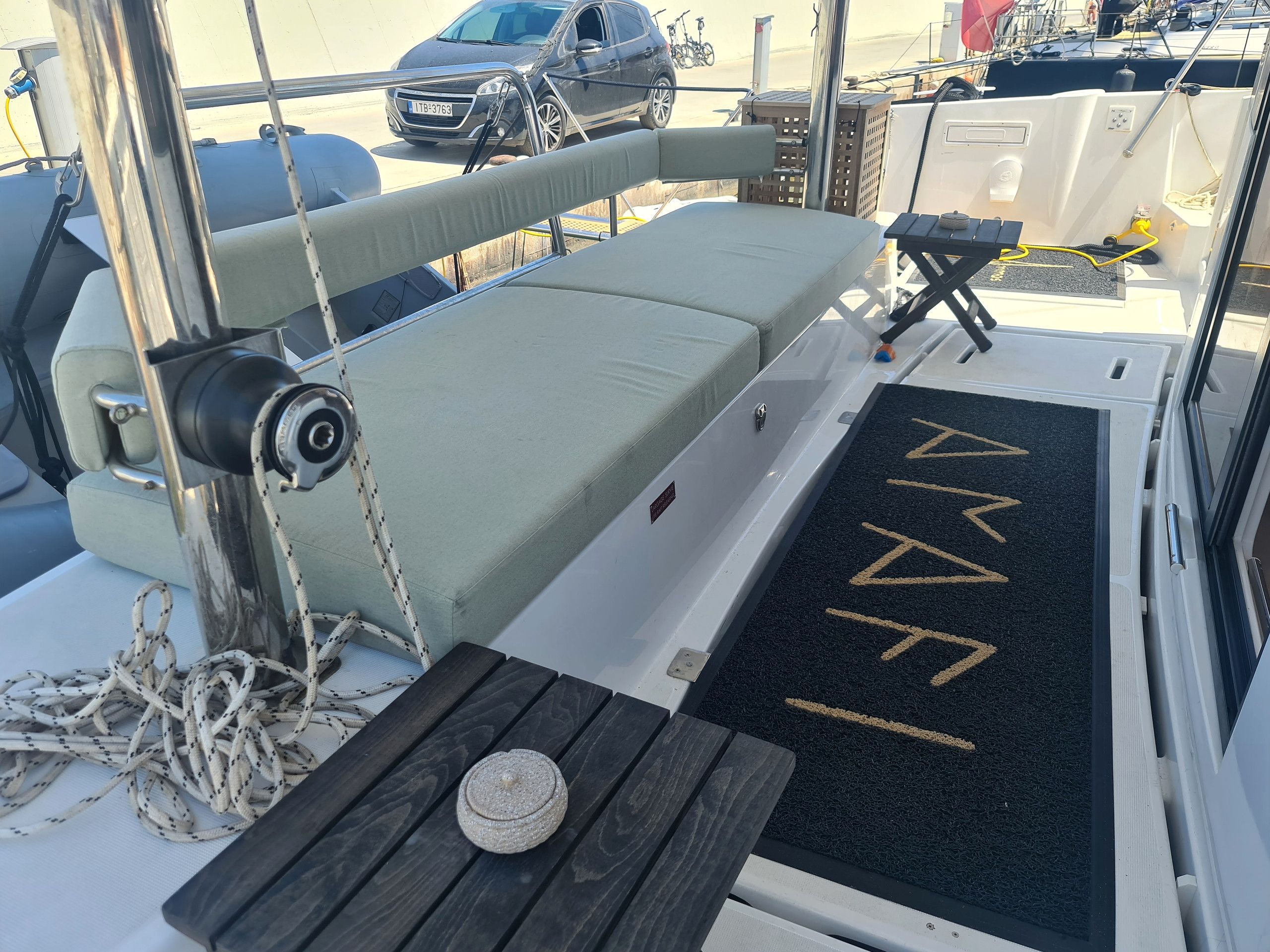 A boat's deck with a cushioned seating area, a small table, and a doormat with a directional arrow.