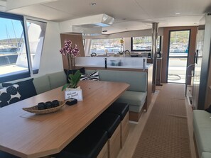 A modern interior with a wooden dining table, a 'Welcome on Board' sign, a potted orchid, and a view of the marina outside.