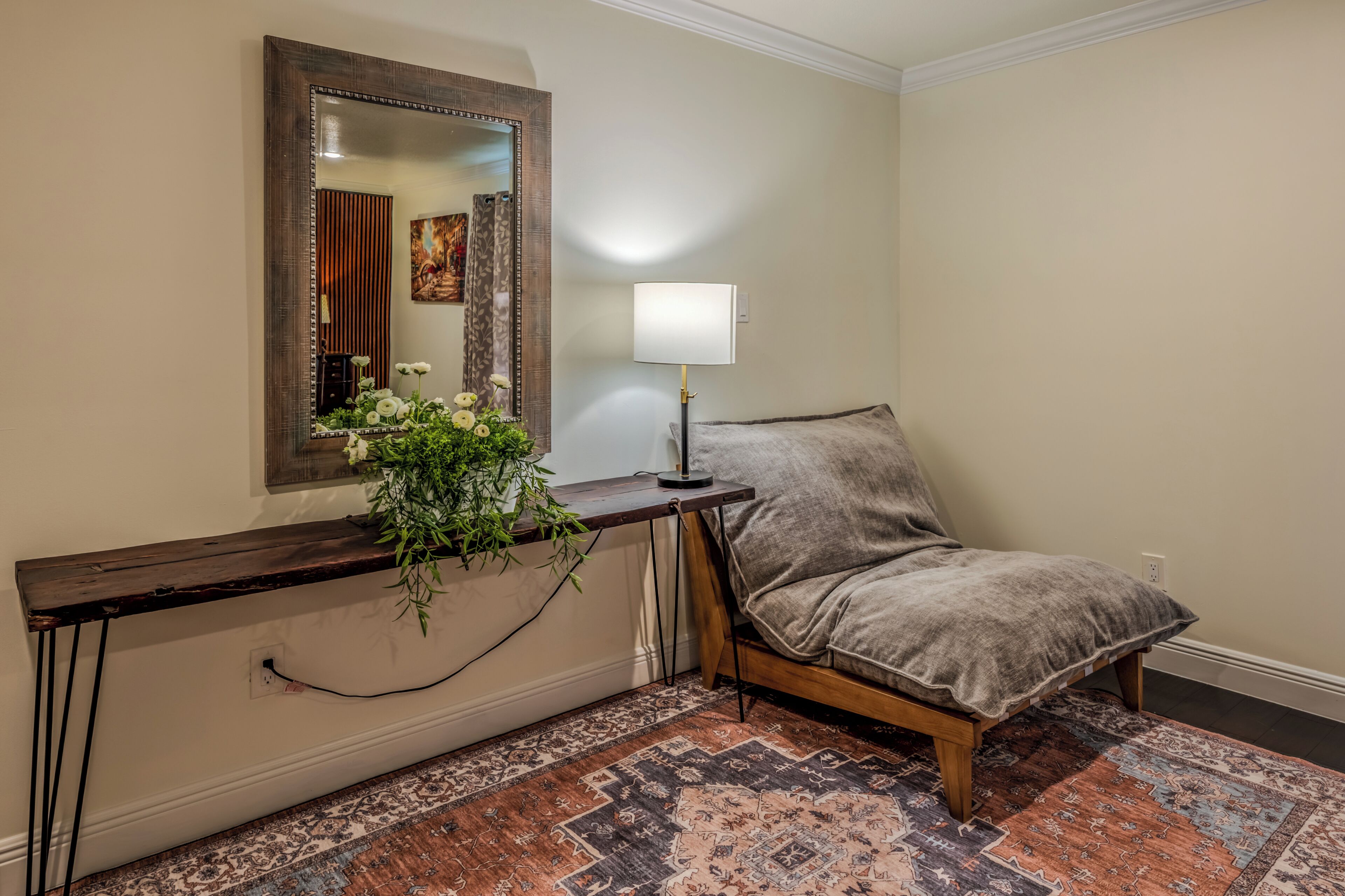 A room with a bed, a bedside table with a lamp, a mirror, and a patterned rug.