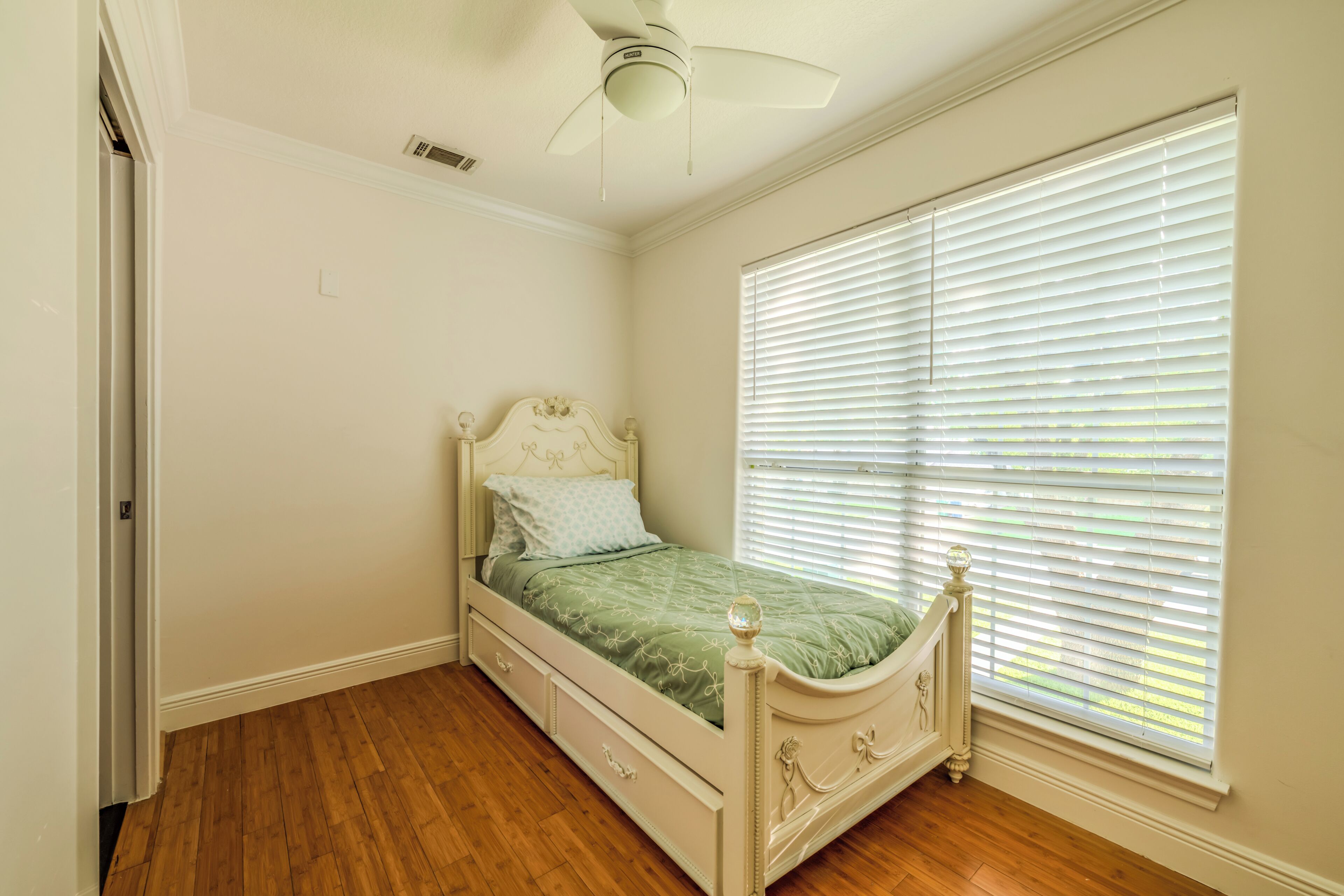 Un dormitorio con una cama individual, ventilador de techo y ventana con persianas.