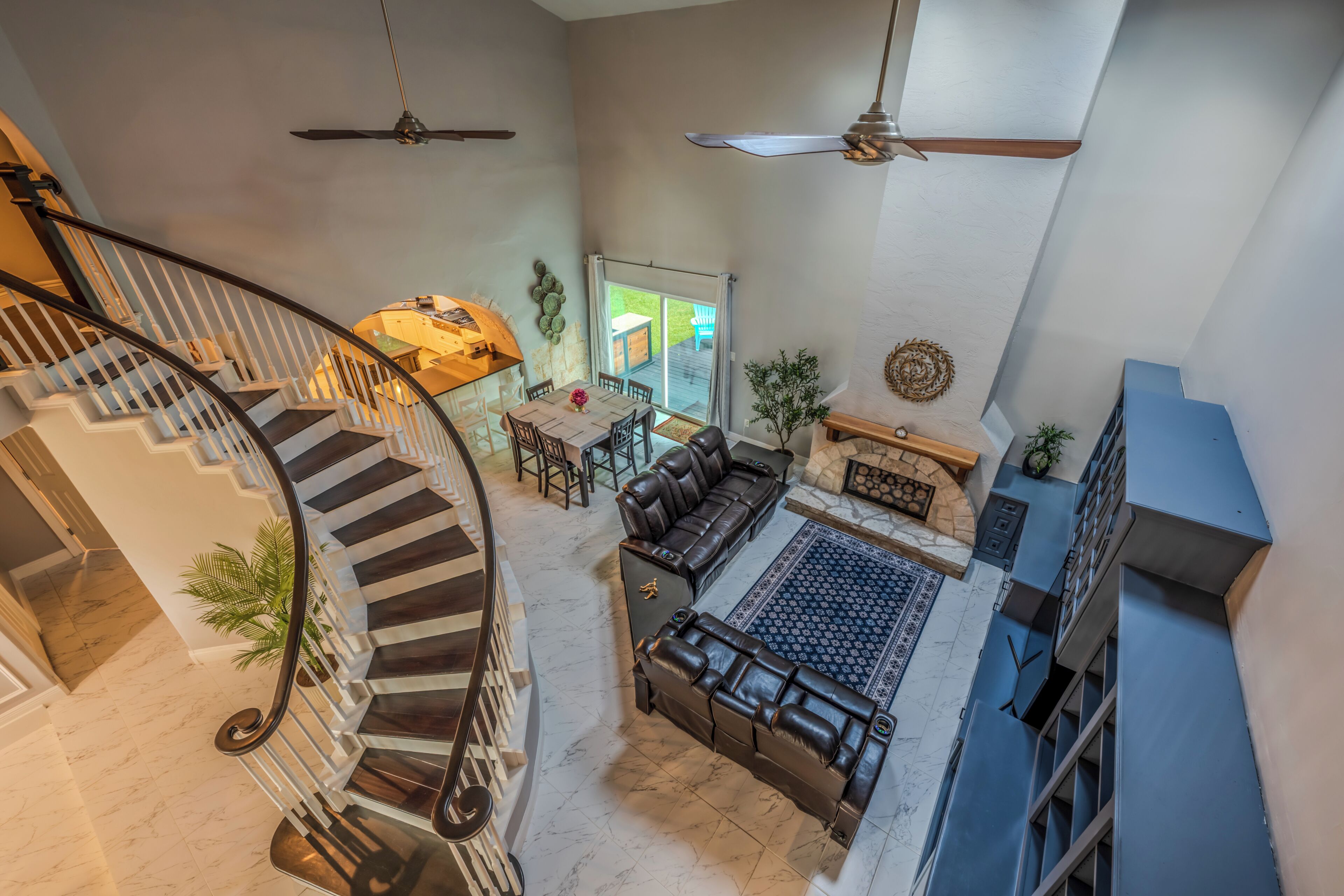 A spacious living area with a fireplace, a dining table, and a staircase with a curved railing.