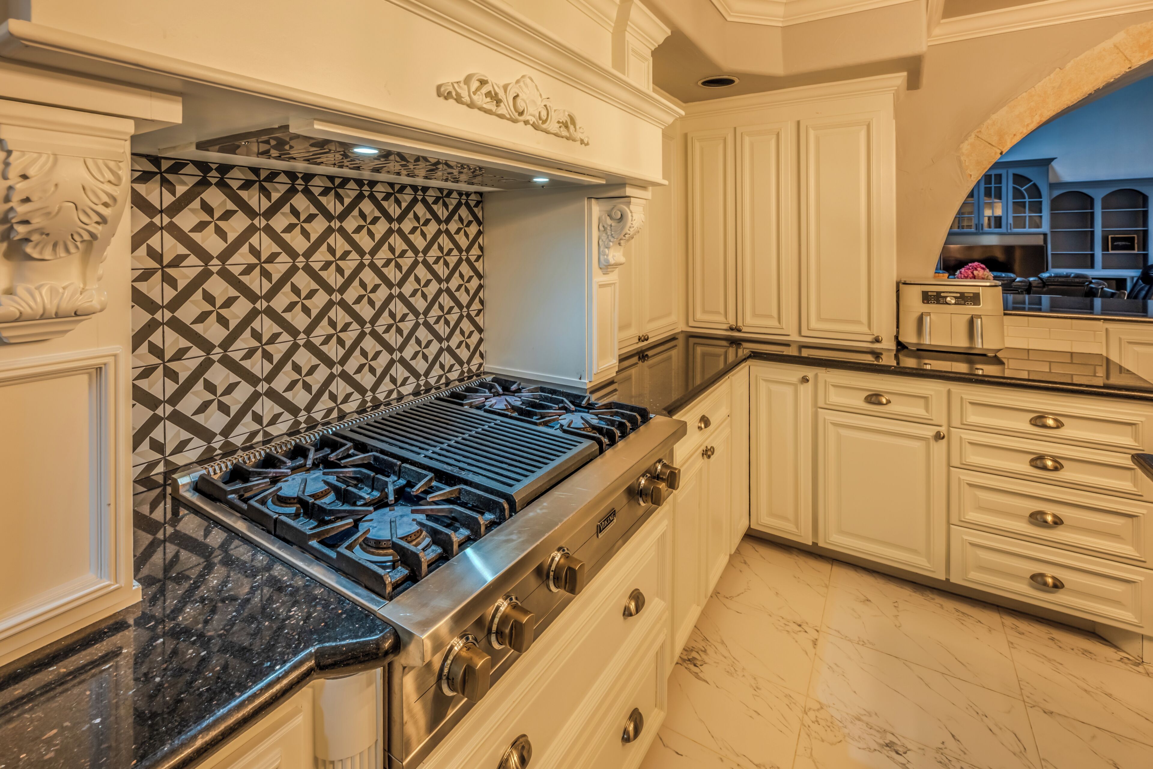 A kitchen with a gas stove, white cabinetry, and a patterned backsplash.