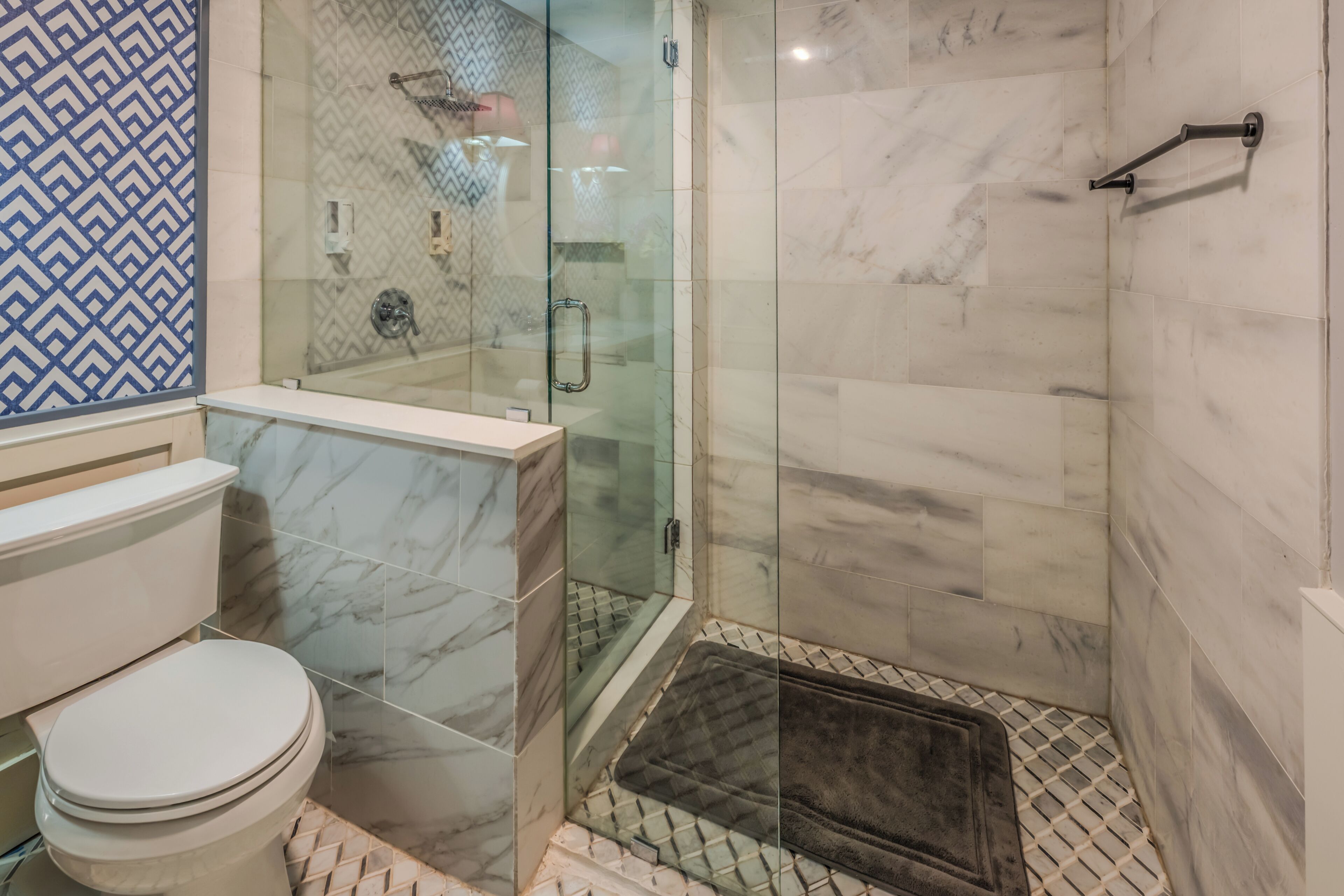 A bathroom with a glass-enclosed shower, a toilet, and a patterned wall.