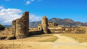 An ancient stone structure with a pathway leading through ruins, surrounded by mountains and a clear sky.