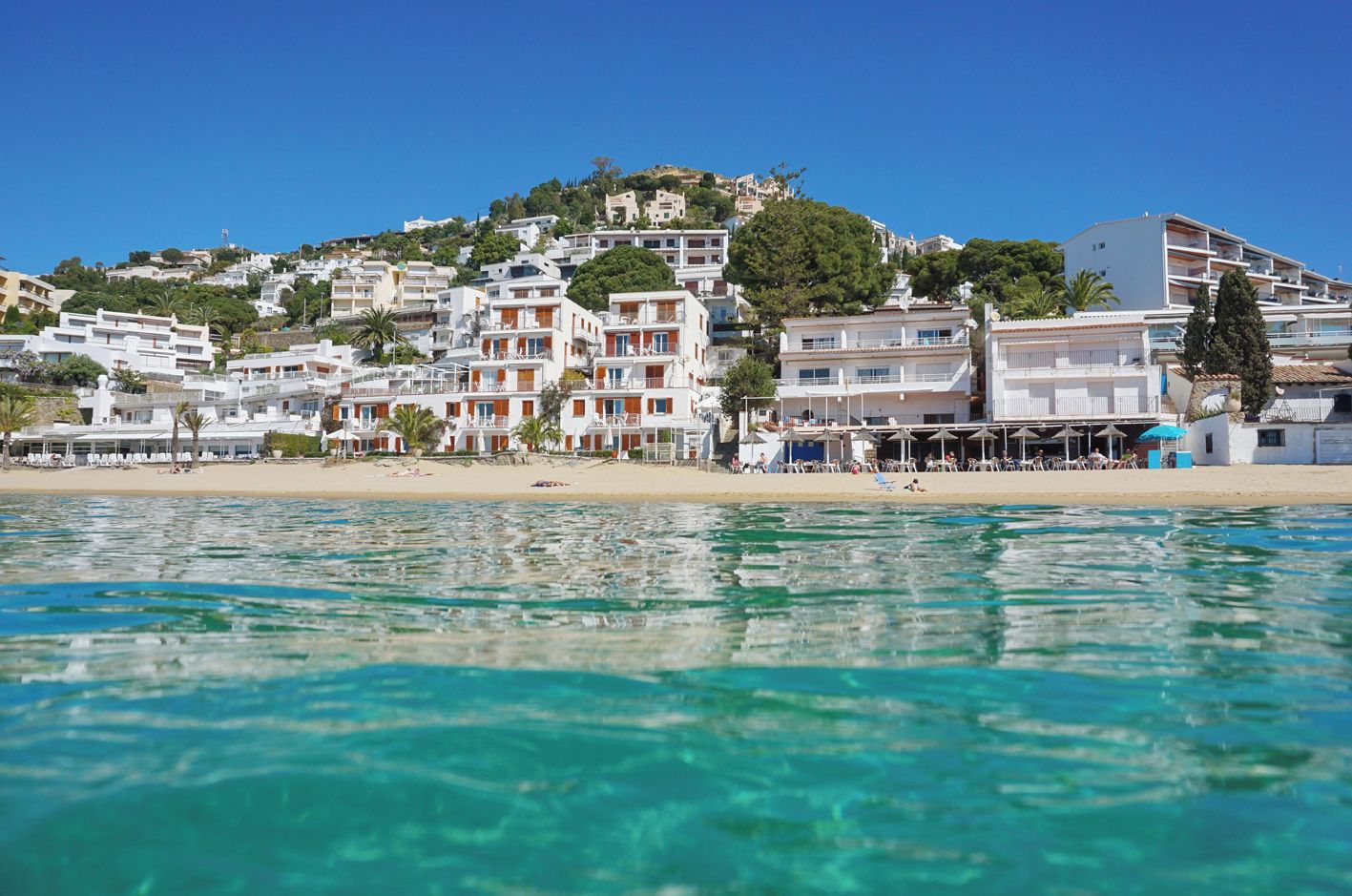 Un hôtel en bord de mer, avec plusieurs étages, situé directement sur la plage et offrant une vue sur des eaux d’un bleu limpide.