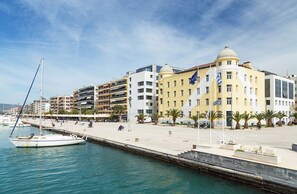 Eine Uferpromenade mit einer Reihe von Gebäuden, einem Steg mit einem Segelboot und Palmen.