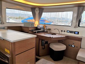 A compact kitchen with a sink, a small countertop, and a window with a view of boats and a blue structure. - Sun-Kissed Sailing Adventure in Islas Sarónicas (Alimos)
