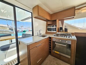 A compact galley kitchen with a stainless steel sink, a stove, and a microwave. - Sun-kissed Sailing Adventure in Split-Dalmatia, Croatia (Seget Donji)