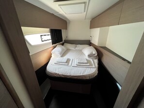 Une cabine compacte et bien éclairée, dotée d’un lit simple, d’une fenêtre avec des rideaux et d’un luminaire au plafond.