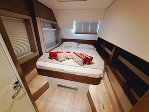 Una habitación pequeña con cama, ventana con persianas, cabecero de madera y una puerta con manija.