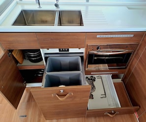 Une cuisine compacte équipée d’un évier, d’un four et de deux appareils noirs, probablement un four à micro-ondes et un grille-pain, placés sous des meubles de cuisine en bois.