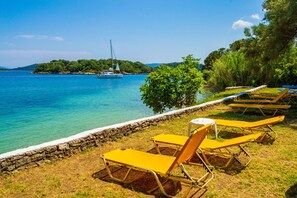 Une vue sur la côte, avec un mur de pierre, des chaises longues jaunes et un voilier à l’horizon.
