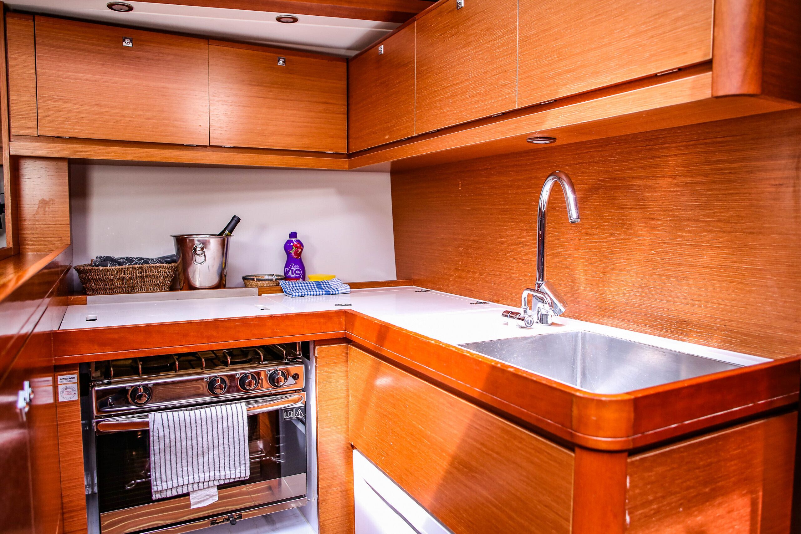 A compact kitchen with wooden cabinetry, a stainless steel sink, and a built-in oven.